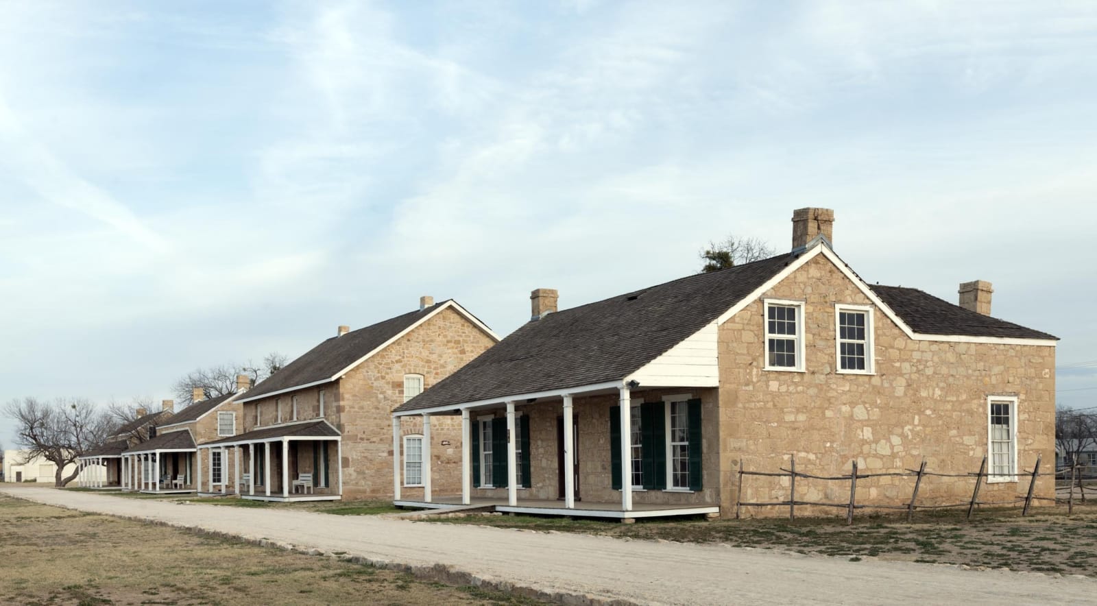 A row of restored limestone quarters with porches and chimneys beside the gravel parade ground at Fort Concho.