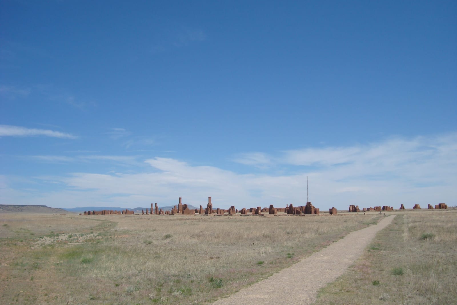 A path across open grassland toward the low adobe ruins of Fort Union under a wide sky