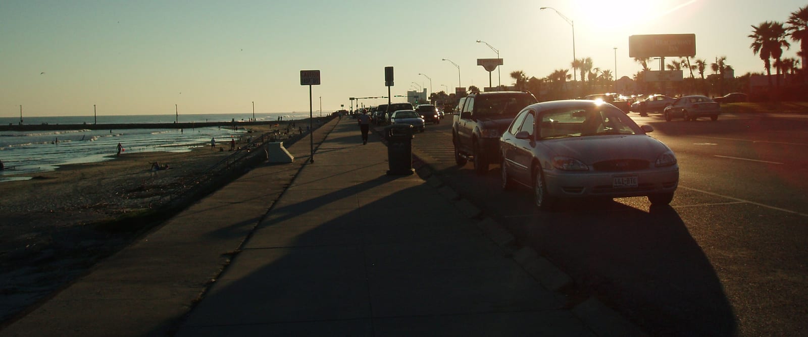 The wide walk along the top of the Galveston seawall at sunset, with the Gulf on one side and parked cars on Seawall Boulevard.
