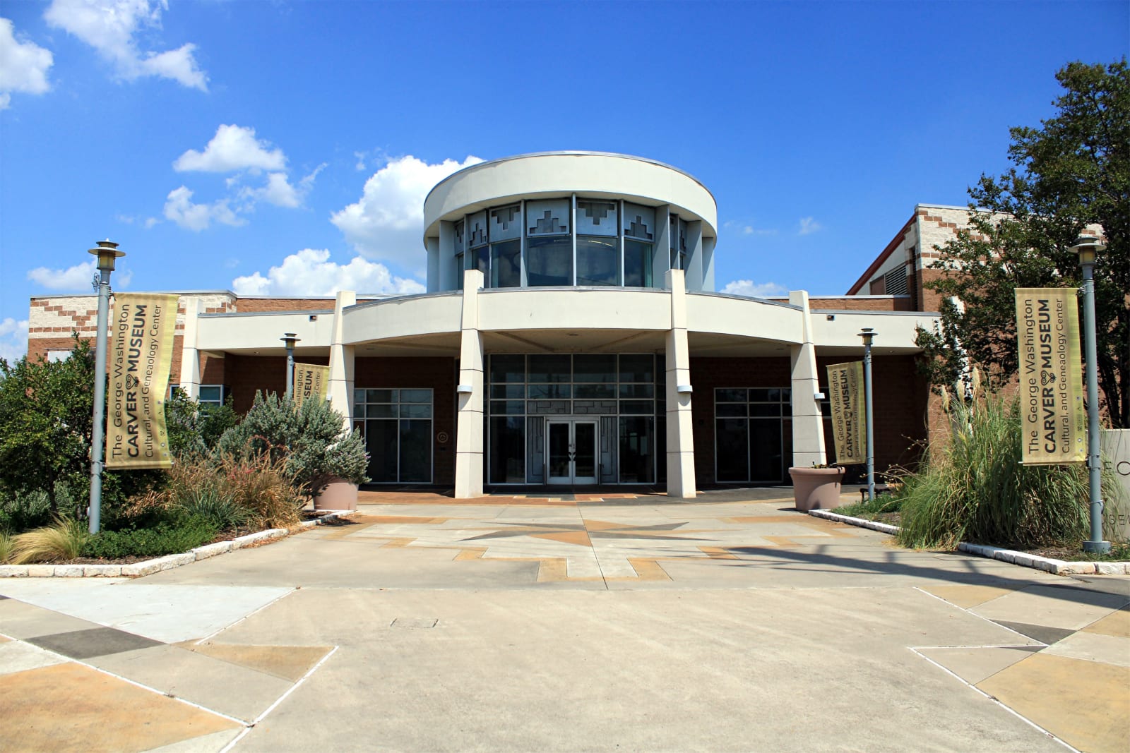 The round glass entry and white columns of the George Washington Carver Museum in East Austin under a blue sky.