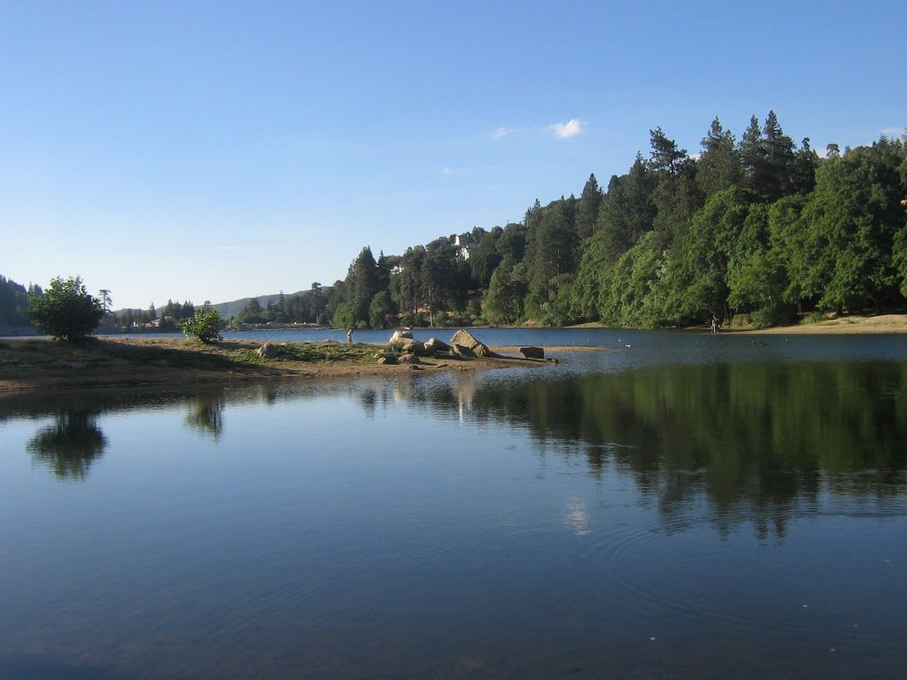 Lake Gregory at Crestline, pines and cabins along the far shore reflected in still water.