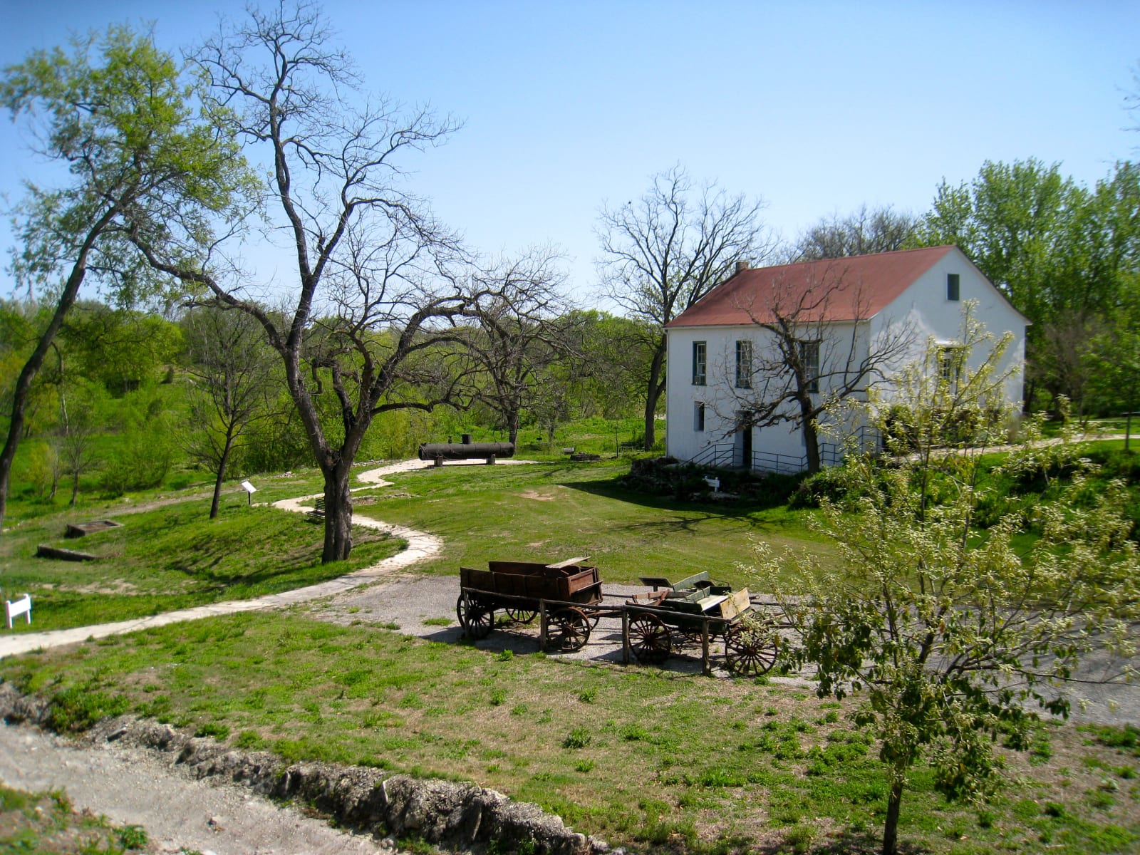 The white two-story Landmark Inn in Castroville seen across a lawn with a curving path and an old wagon in the shade.