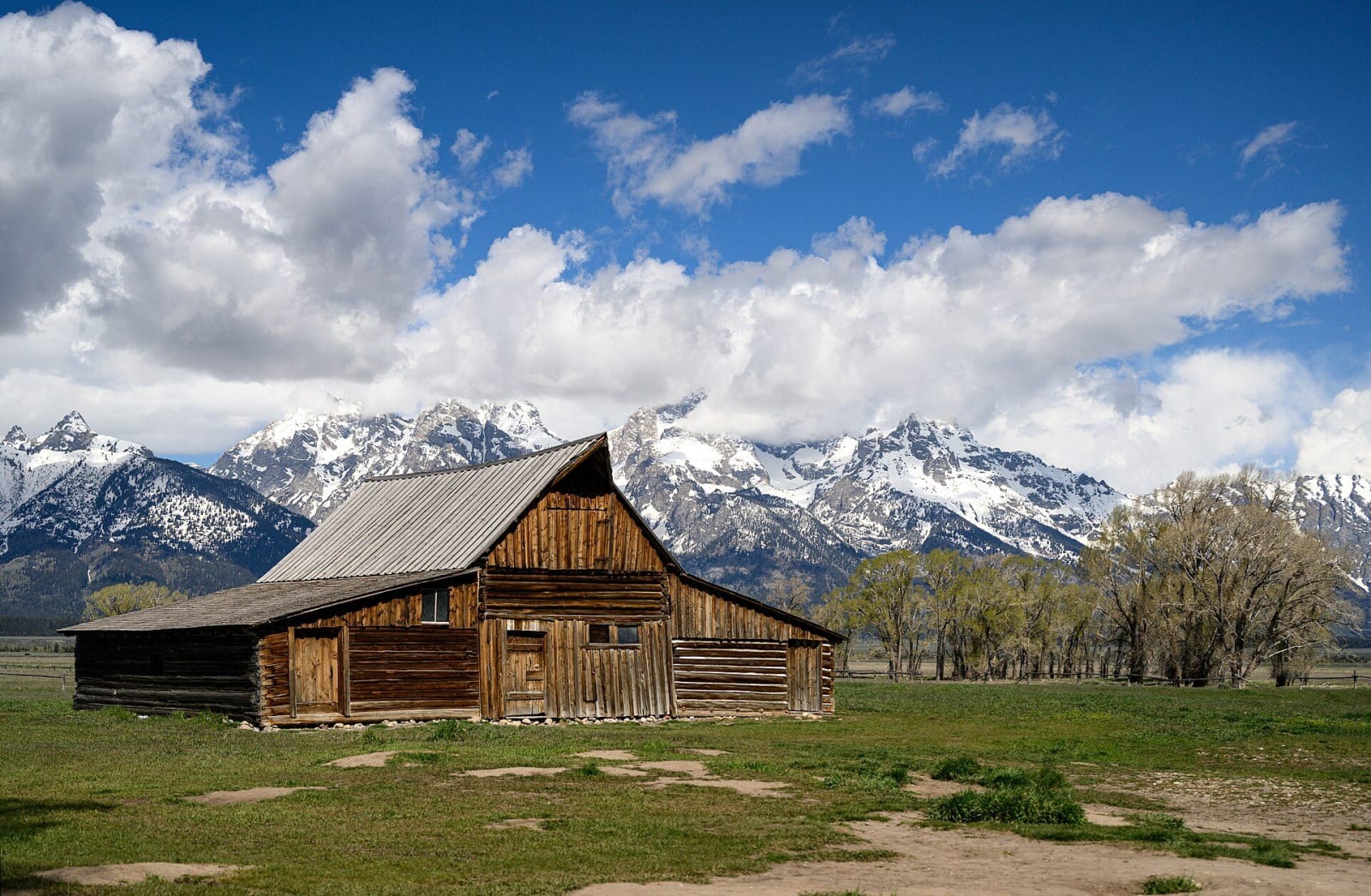 A weathered gambrel-roofed Moulton barn on Mormon Row, snowy Teton peaks half hidden in cloud behind it