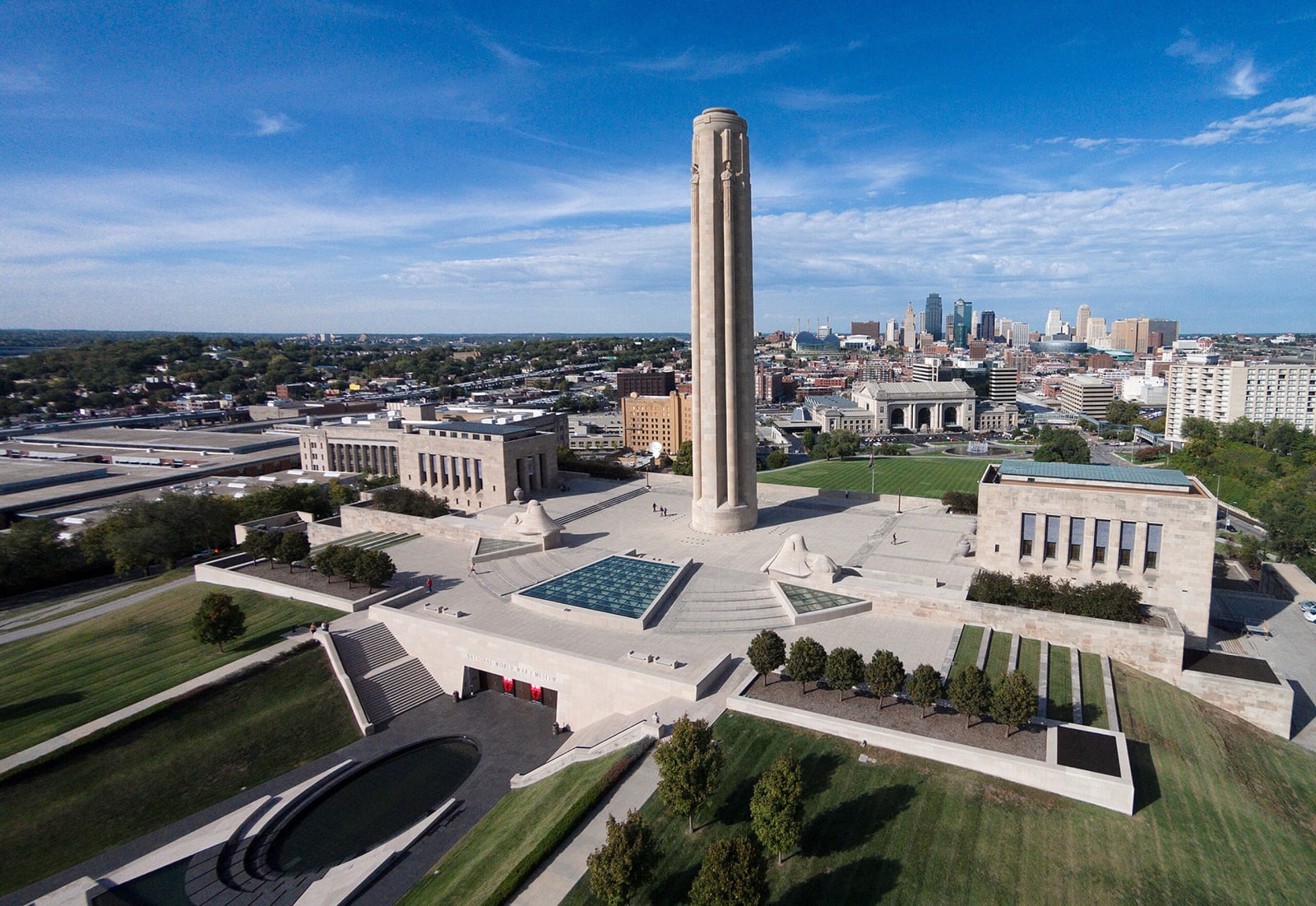 An aerial view of the Liberty Memorial tower and its two flanking halls, with the downtown Kansas City skyline behind.