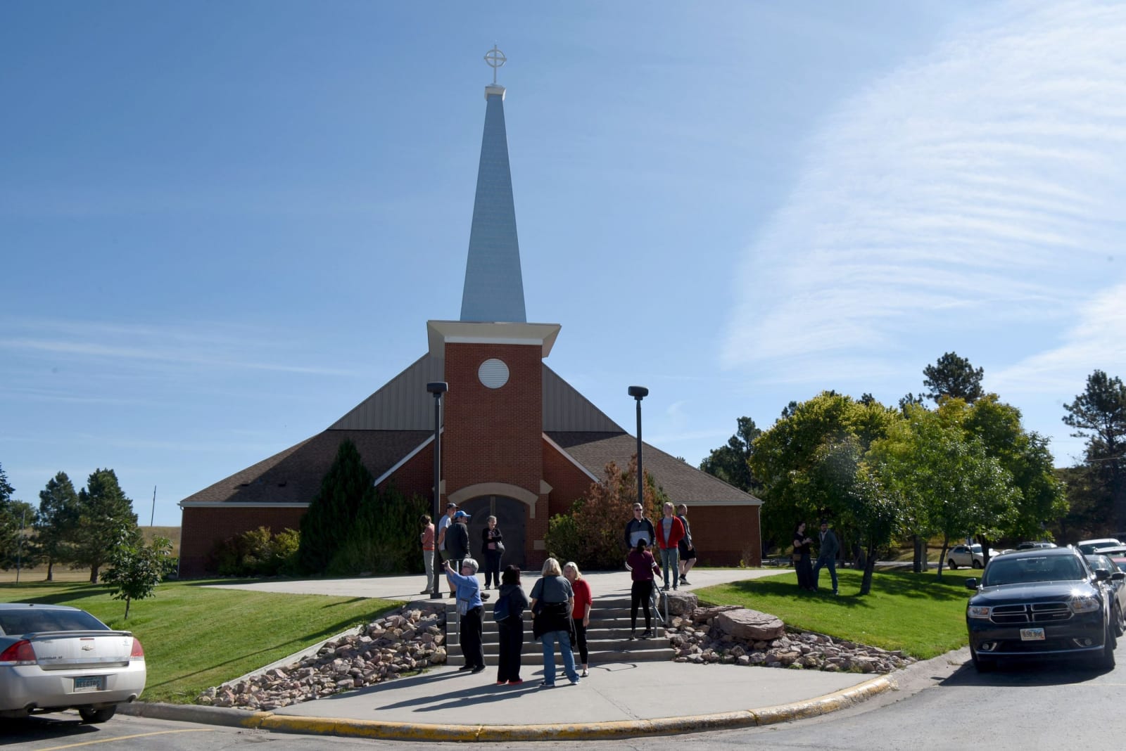 Holy Rosary Catholic Church at Red Cloud Indian School, a brick church with a tall white steeple, with visitors gathered at the front steps
