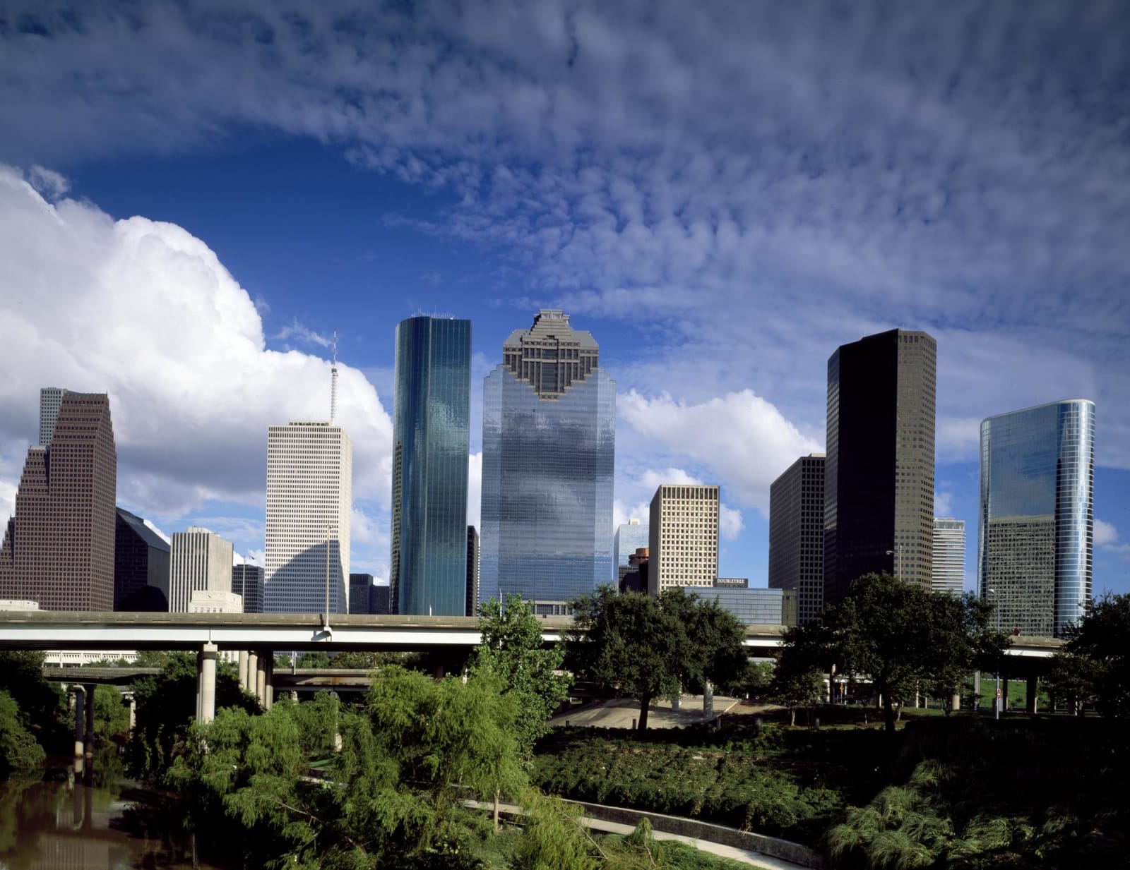 The glass towers of downtown Houston rising above the trees and lawns of Sam Houston Park.