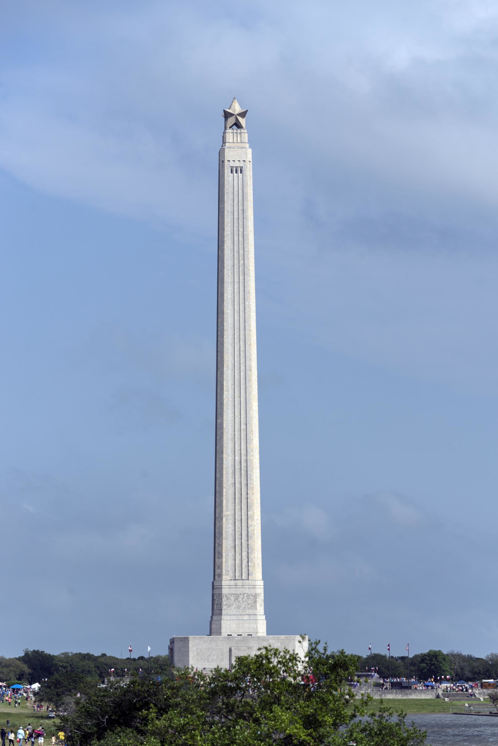 The San Jacinto Monument, a tapering stone shaft topped by a star, rising above trees against a blue sky.