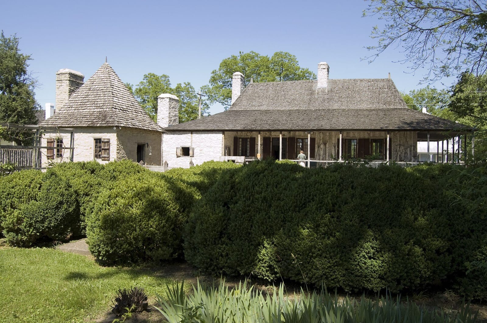 The Bolduc House and its detached kitchen with steep hipped roofs and a wide gallery behind a garden in Ste. Genevieve.