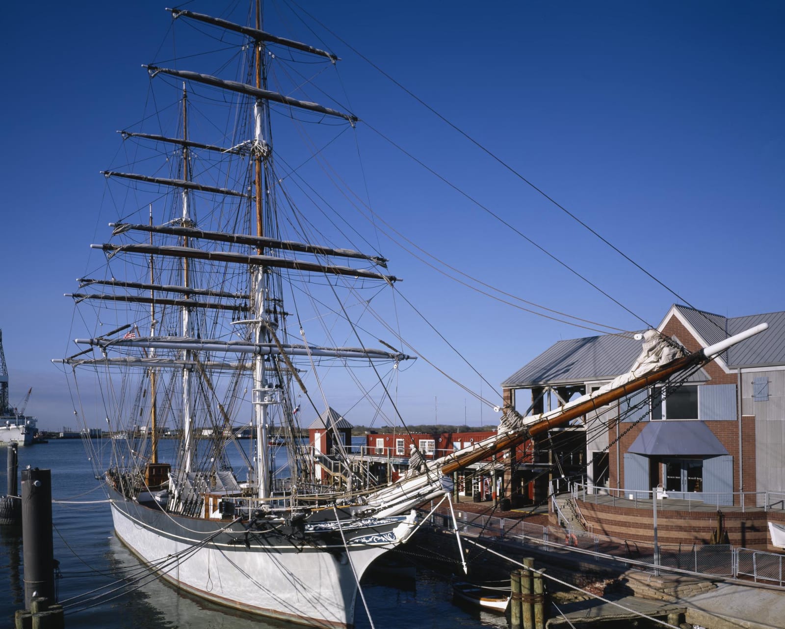 The three-masted barque Elissa moored at her pier in Galveston, her rigging and yards against a deep blue sky.