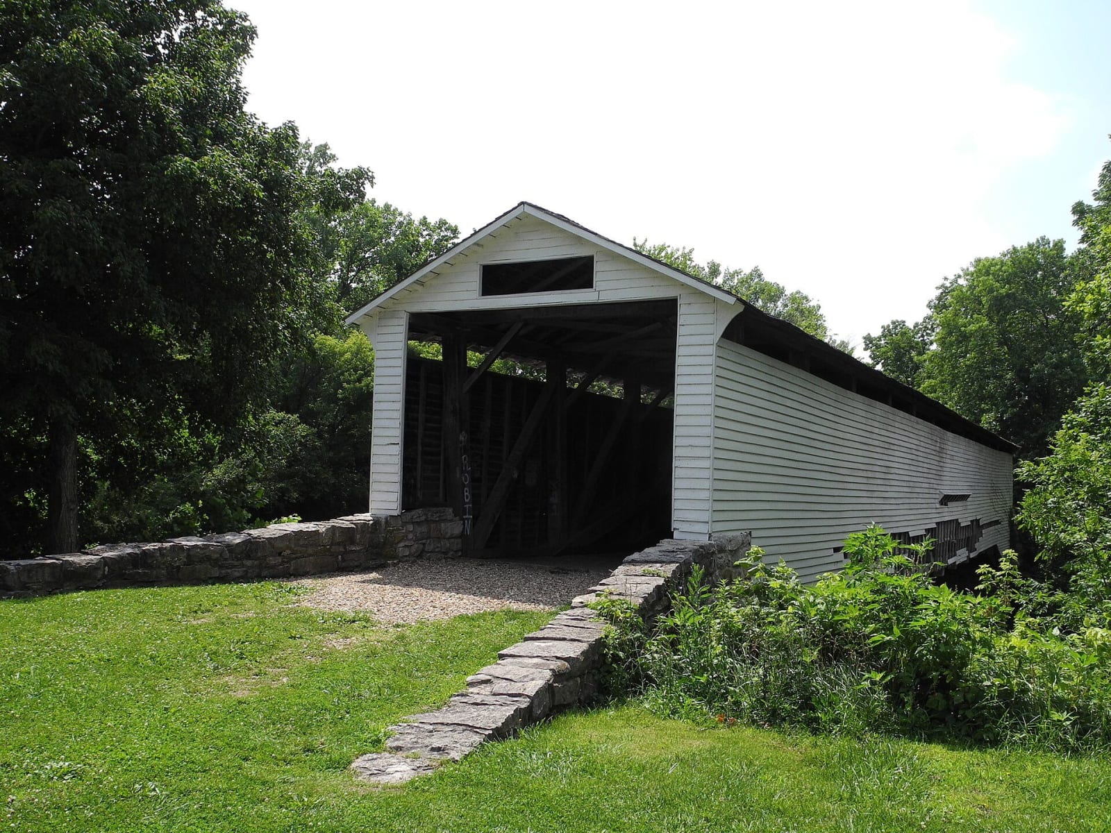 The white Union Covered Bridge on its stone abutment among summer trees.
