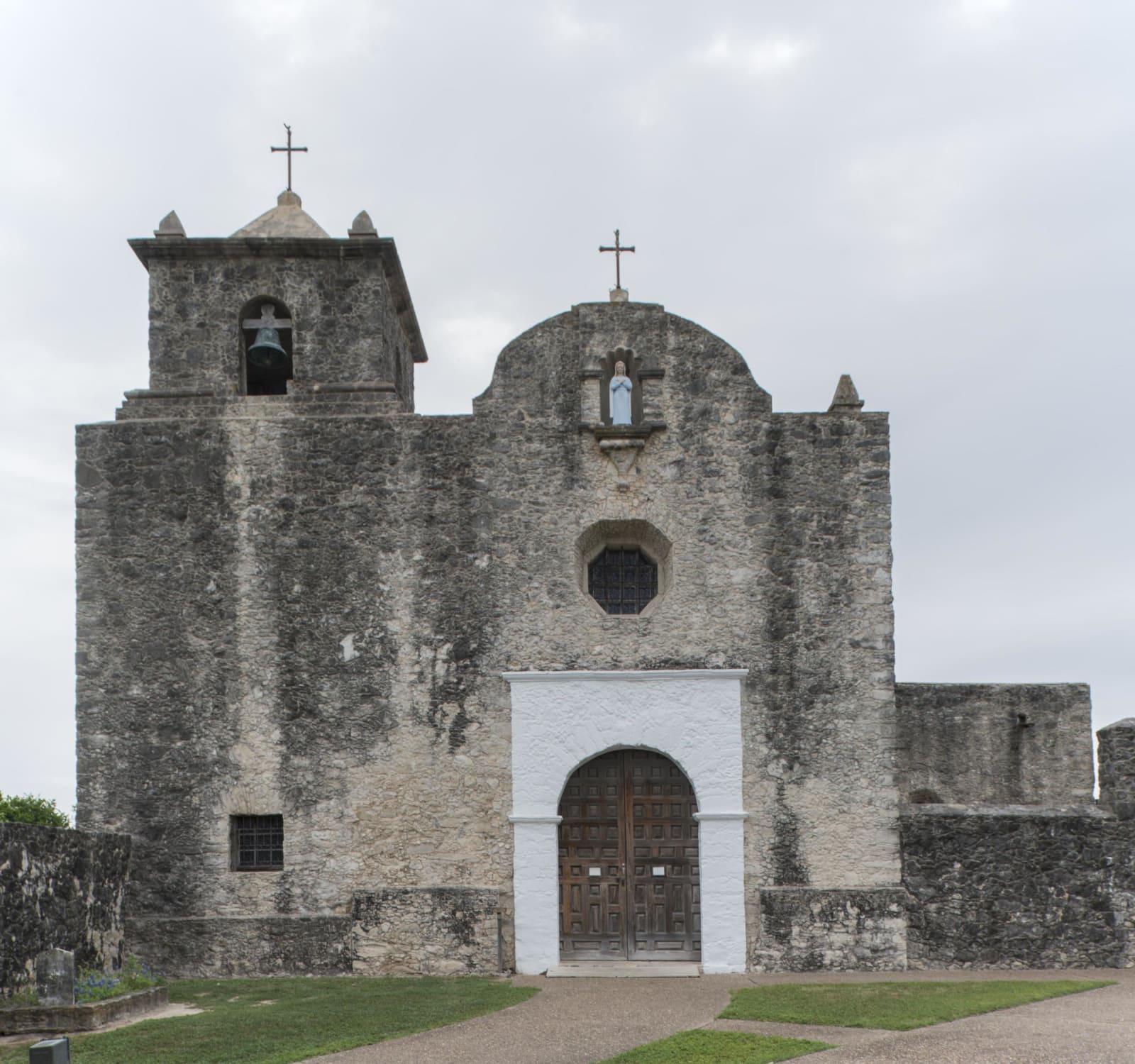 The weathered limestone front of the Our Lady of Loreto chapel at Presidio La Bahia in Goliad, with its bell tower and arched wooden door.