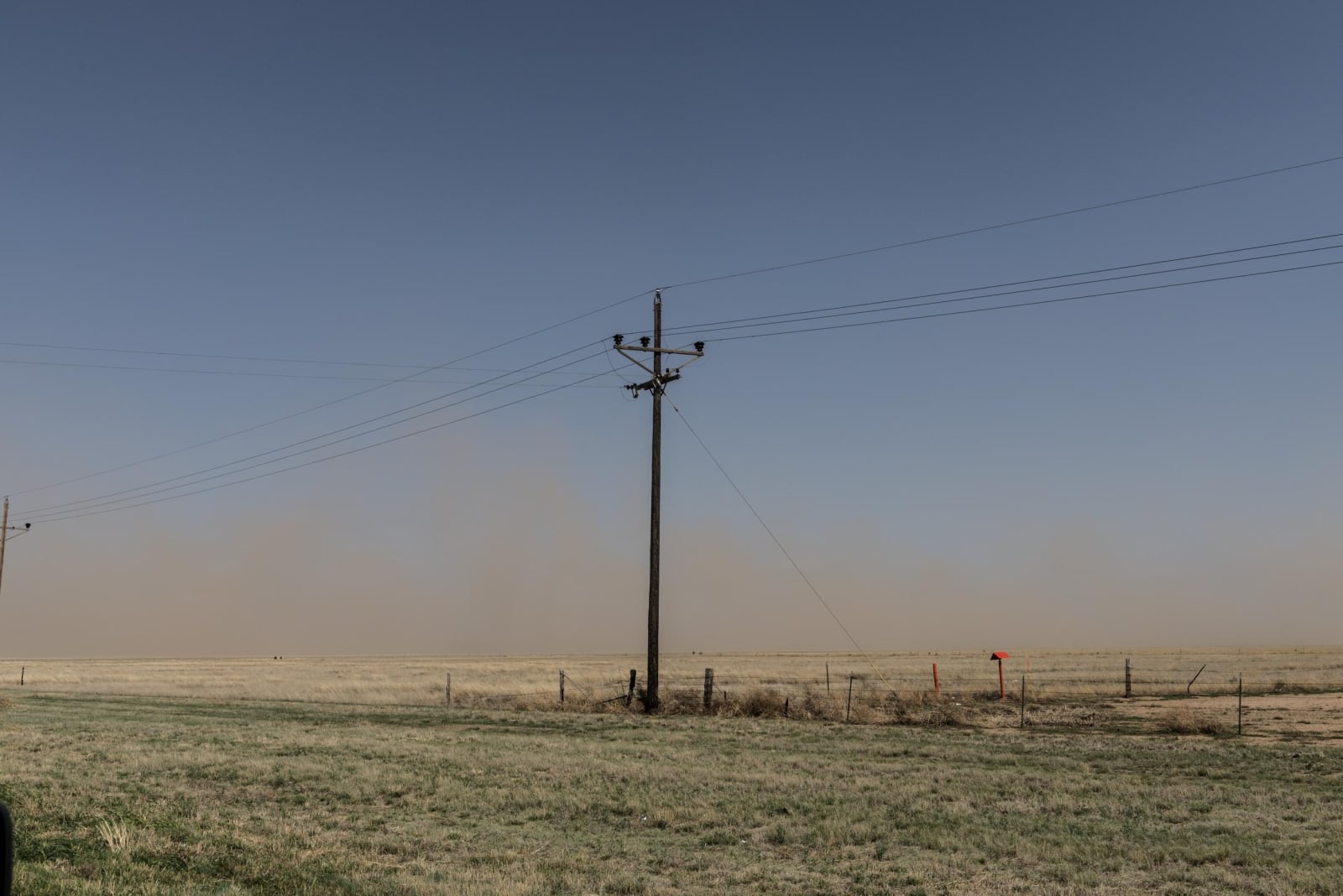 A haze of blowing dust hanging over flat grassland and a line of power poles along U.S. 60 east of Amarillo.