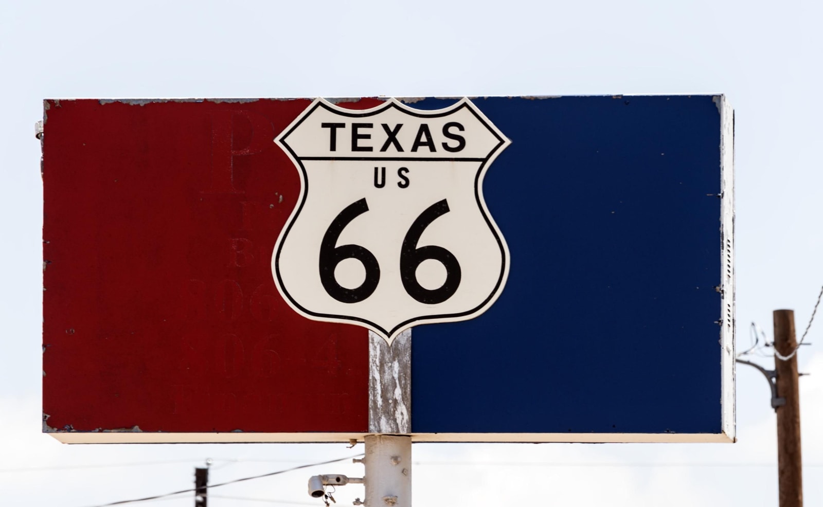 A Texas US 66 highway shield on a red and blue sign against a pale sky in Amarillo.