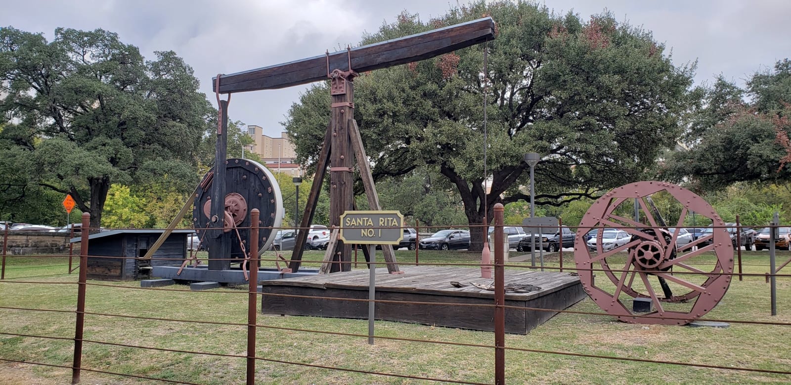The Santa Rita No. 1 cable-tool rig on display on the University of Texas campus in Austin, with its wooden walking beam and iron wheels behind a low rail fence.