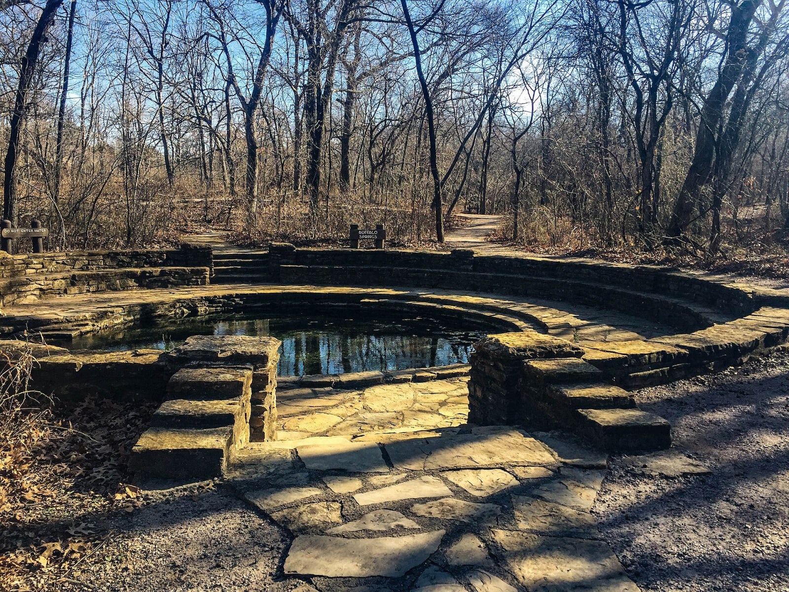 A stone-walled spring pool among bare winter trees in Chickasaw National Recreation Area at Sulphur.