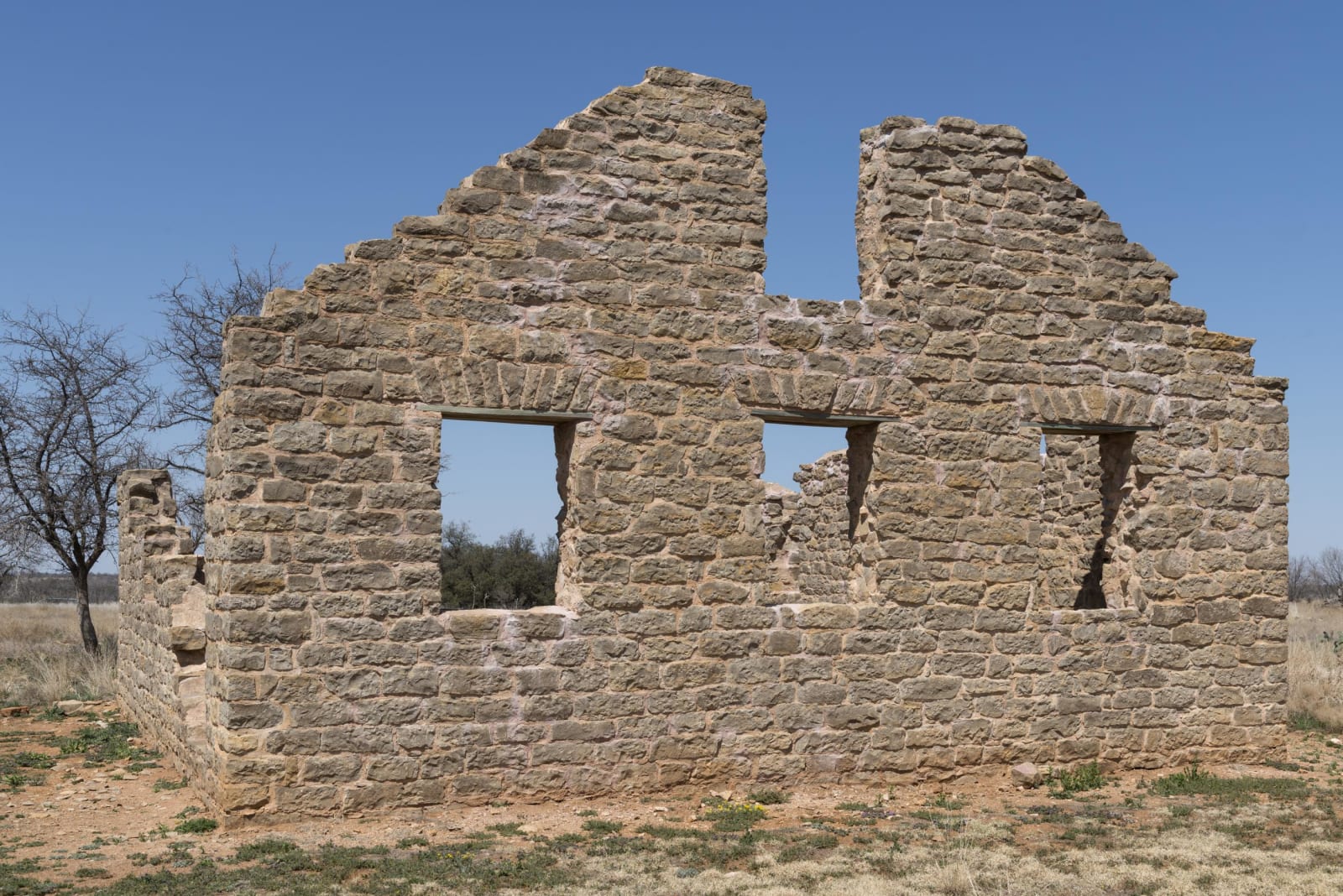 A roofless stone wall with three empty window openings, a ruin of the Army post at Fort Griffin State Historic Site in Shackelford County.