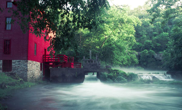 The red Alley Mill beside the rushing blue-green outflow of Alley Spring under summer trees.