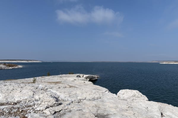 Pale limestone ledges at the edge of Amistad Reservoir, with deep blue water stretching to low distant shores.