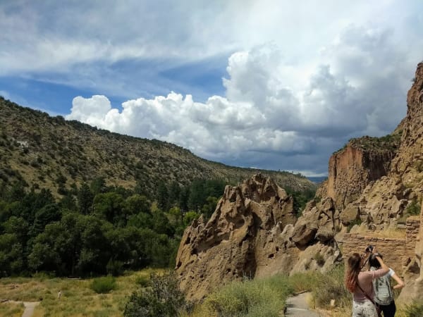 Eroded tuff cliffs in Frijoles Canyon at Bandelier, looking up the canyon toward the Jemez Mountains, a visitor taking a photograph in the foreground