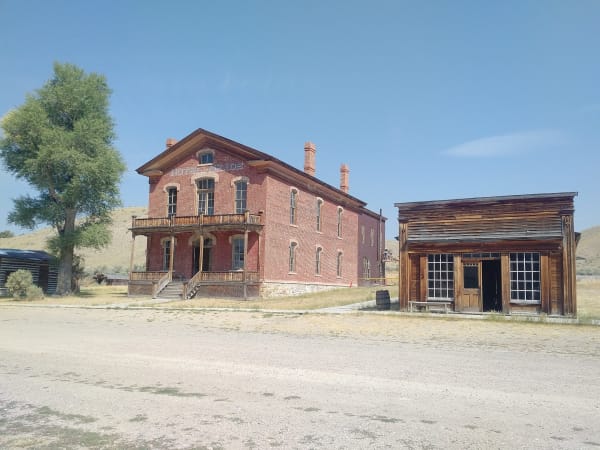 The red-brick Hotel Meade at Bannack, two storeys with a balcony over the door, beside a weathered false-front saloon on the dirt street