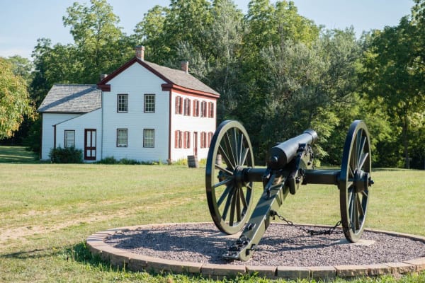 A cannon on a gravel circle before the white Thome-Benning House at Battle of Athens State Historic Site.