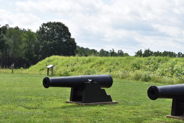 Two iron cannons on the grass below the grassy earthen walls of Fort Davidson at Pilot Knob.