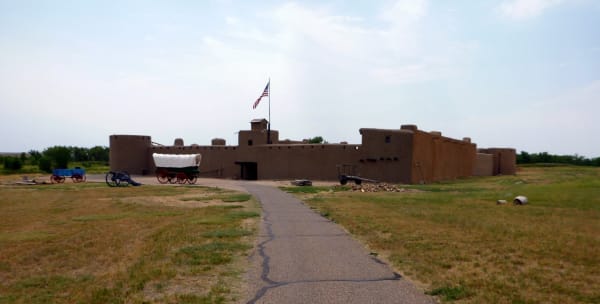The reconstructed adobe walls of Bent's Old Fort across the grass from the approach path