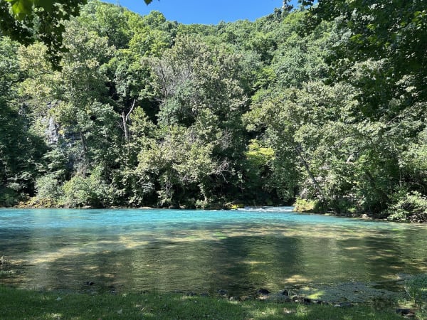 The turquoise pool of Big Spring at the foot of a wooded bluff in summer.