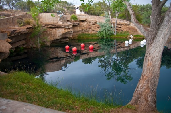 The still blue water of the Blue Hole in Santa Rosa, ringed by sandstone ledges, a cottonwood and floating dive buoys