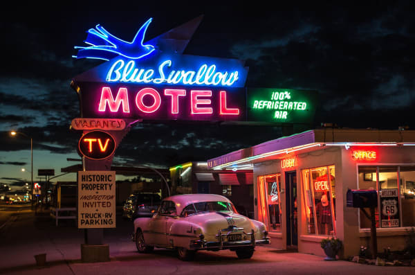 The Blue Swallow Motel's neon sign glowing at dusk on Route 66 in Tucumcari, an old car parked by the office