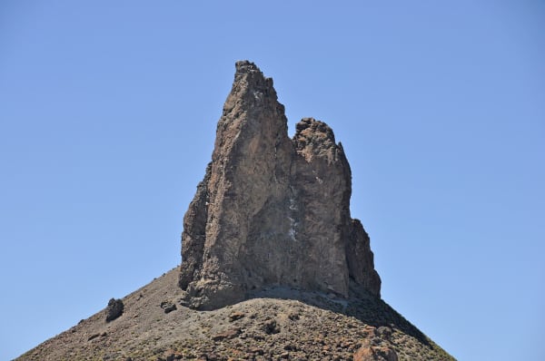 Boars Tusk, a jagged dark volcanic spire rising from a slope of loose rubble against a clear blue sky