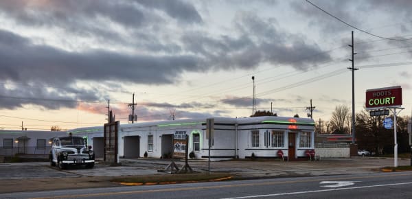 The white Streamline Moderne Boots Court motel and its red neon sign at dusk on Route 66 in Carthage.