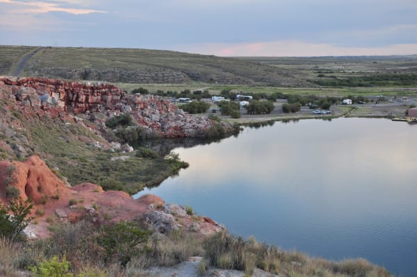 A still lake below red bluffs at Bottomless Lakes State Park, a campground on the far shore