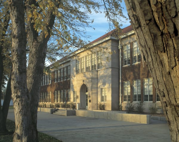 Monroe Elementary School in Topeka, a two-story brick and limestone building, seen past tree trunks in late-afternoon light.
