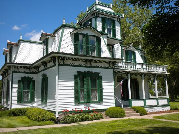 The white Second Empire house at Scout's Rest, with green shutters and a cupola, stands behind flower beds in North Platte.