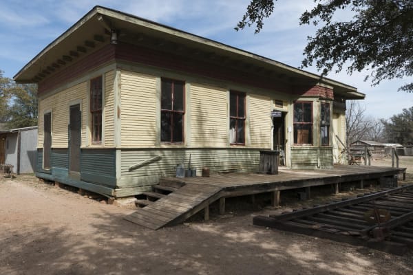 The wooden railroad depot at Buffalo Gap Historic Village, painted cream and green with a red band, with a plank platform and a short length of track in front.