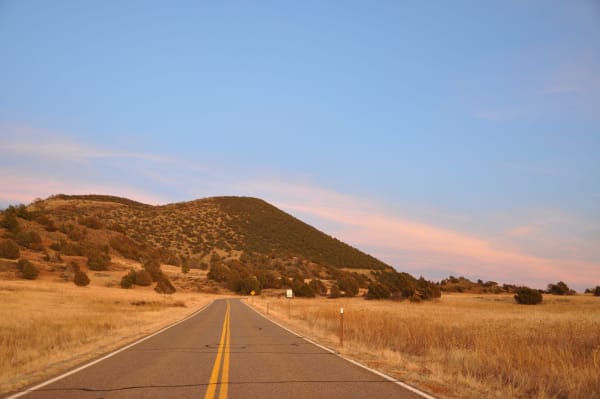 The entrance road running through golden grass toward the cinder cone of Capulin Volcano at sunset