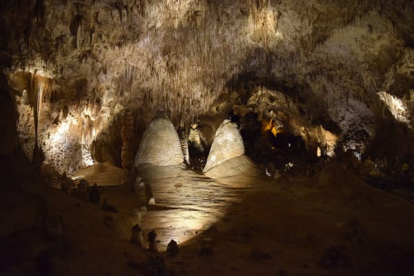 Two domed stalagmites lit in the dim vault of the Big Room at Carlsbad Cavern, formations hanging from the ceiling