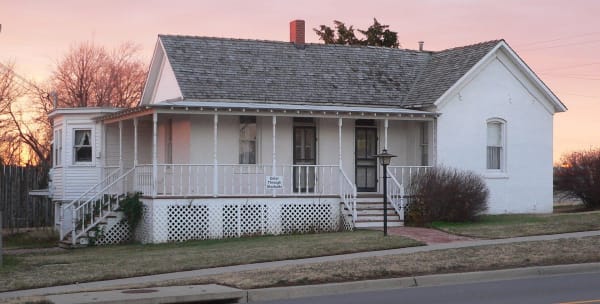 The white one-story Carry A. Nation house in Medicine Lodge with its long front porch, at dusk.