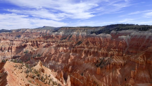 The eroded amphitheater of Cedar Breaks National Monument in southern Utah, its pink and orange rock spires dropping away below a forested rim under a clear summer sky.