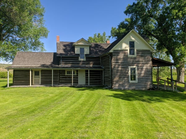 Chief Plenty Coups's two-storey log house in the Pryor Valley, a white-trimmed gable and long porch on a mown lawn under cottonwoods