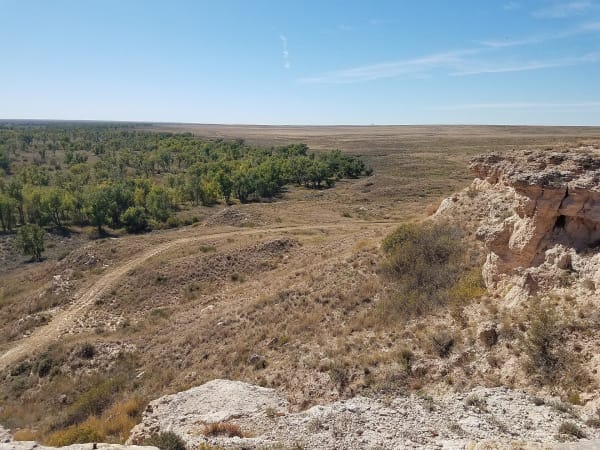 From the caprock of Point of Rocks, the view falls over cottonwoods along the Cimarron River and a faint trail trace across the grassland.