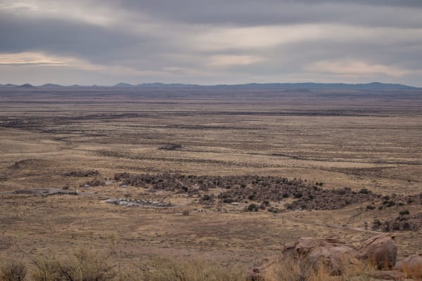 The rock formations of City of Rocks State Park seen from Table Mountain as a dark band across the wide grassland, mountains on the horizon