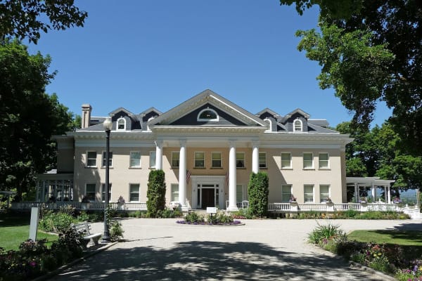The Daly Mansion, a cream Georgian Revival house with a white-columned portico and dormered roof, behind a curved drive and summer gardens
