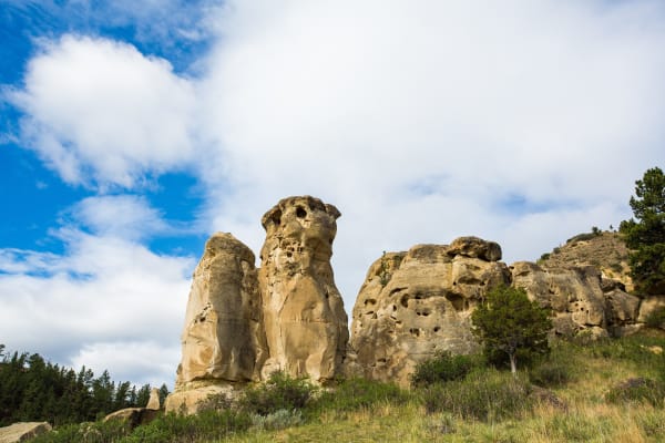 The weathered sandstone pillars of Deer Medicine Rocks, pocked and rounded, rising from grass and sage under a broken summer sky