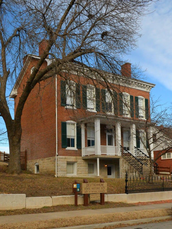 A two-story brick house with a columned porch and green shutters at Deutschheim State Historic Site in Hermann.