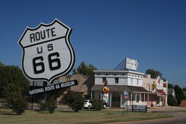A large Route 66 shield sign in front of the museum buildings of the Elk City complex.