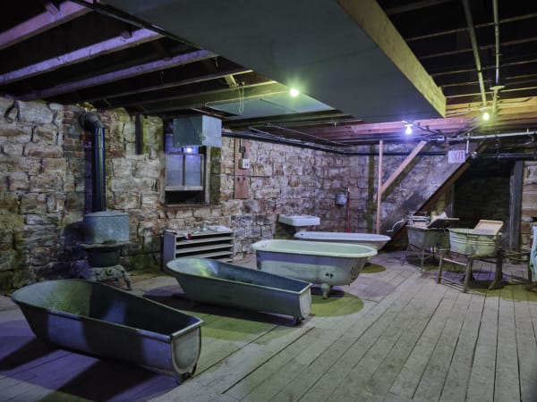 Old bathtubs on a plank floor in a stone-walled room beneath the sidewalks of Ellinwood, part of the underground bathhouse and barbershop.