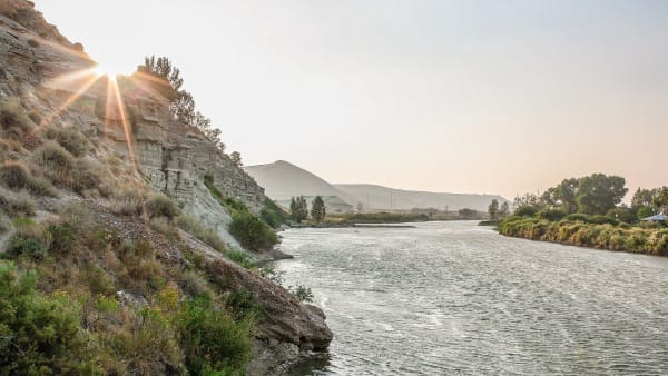 The Green River flowing past Expedition Island in the town of Green River, the sun low over a sagebrush bluff and cottonwoods along the far bank