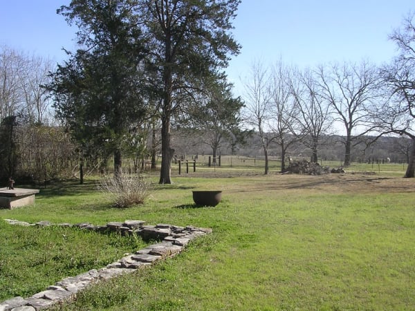The grounds of the Fanthorp Inn site in Anderson: a grassy yard with a low stone border and a tall pine, with bare trees beyond.